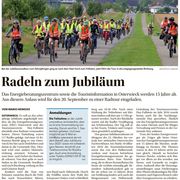 Eine Gruppe von Radfahrern mit Warnweste und Fahrradhelm radelt zum Fallstein. Im Hintergrund sind die Häuser eines Dorfes zu sehen.